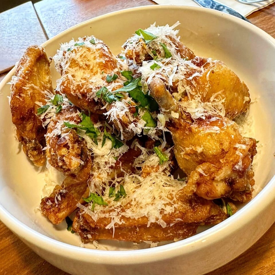 Crispy chicken wings topped with grated Parmesan cheese and fresh herbs in a white bowl.