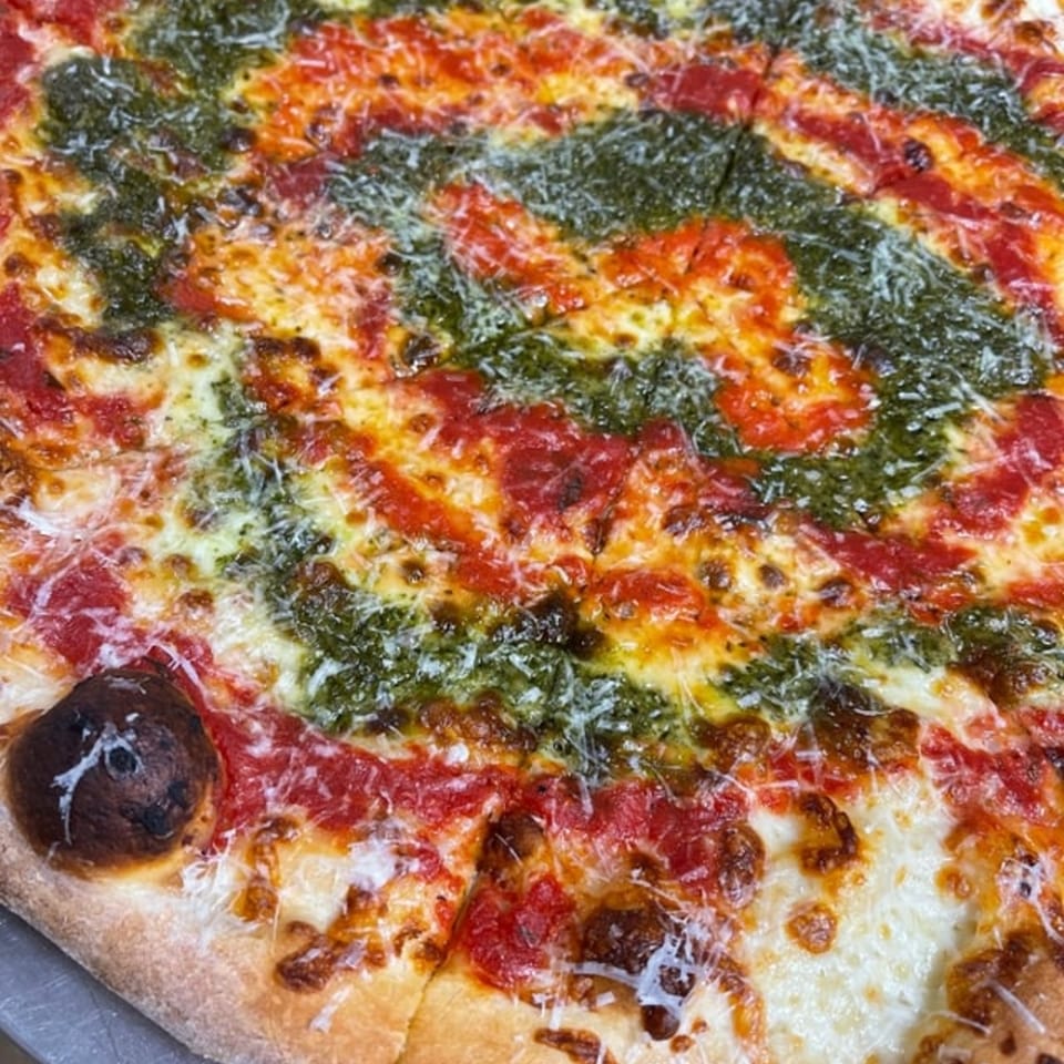 Close-up of a Pizza Wheel Brick Oven pizza with alternating stripes of red sauce and green pesto.