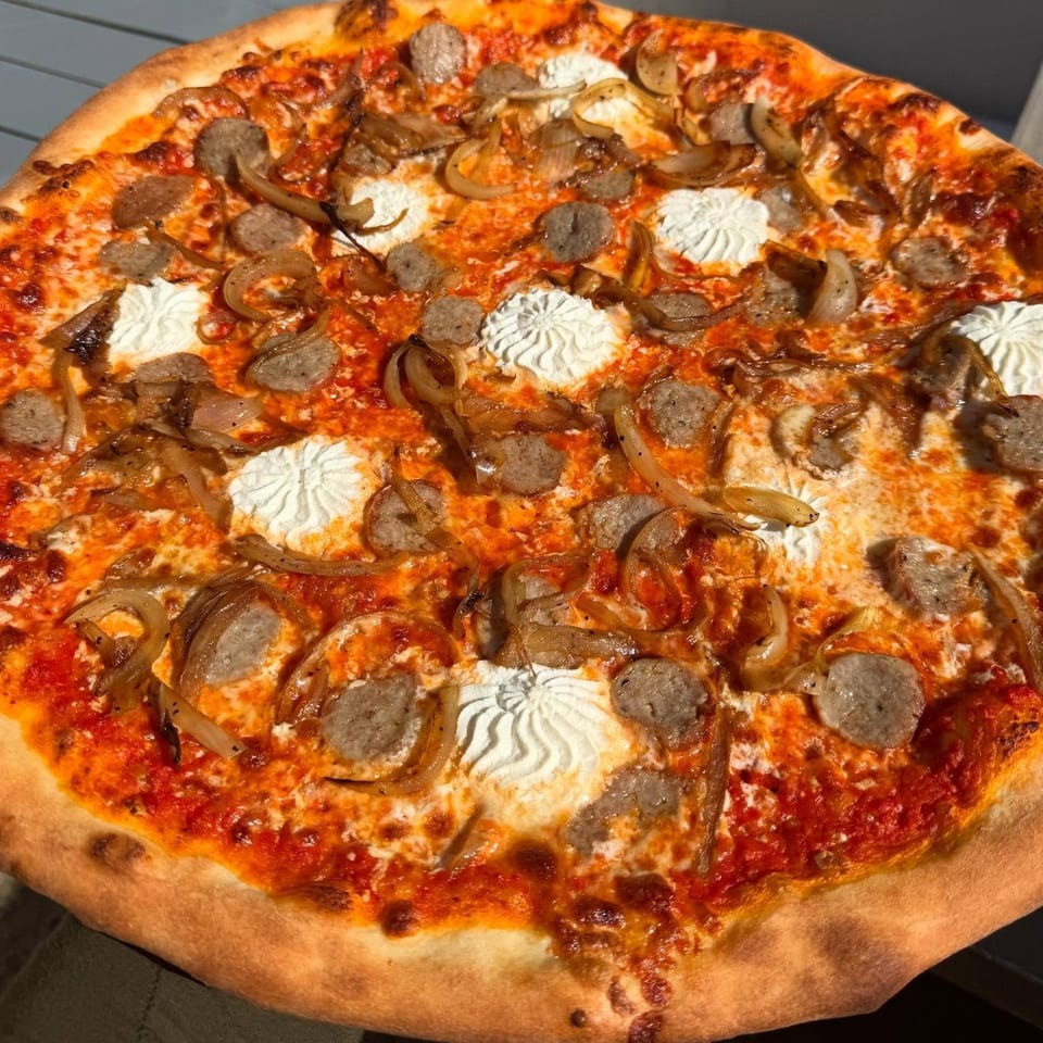 A Pizza Wheel Brick Oven pizza with sausage, caramelized onions, and dollops of ricotta cheese.