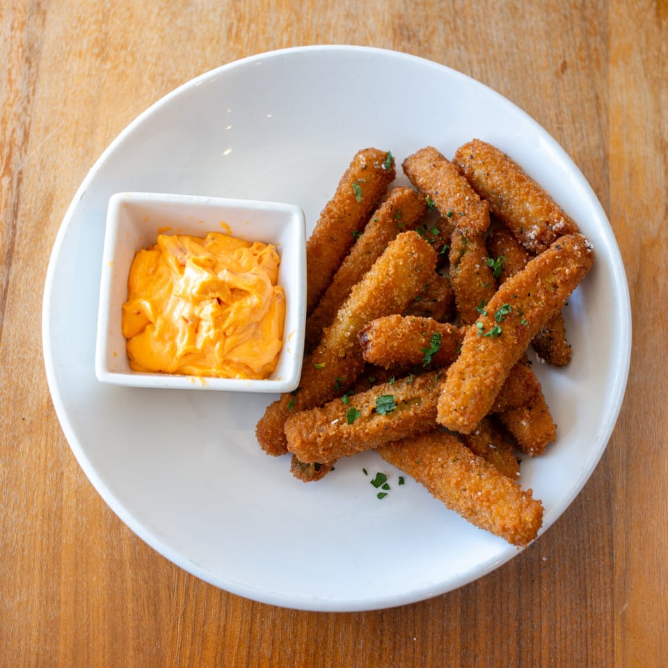 Crispy fried mozzarella sticks with a side of orange dipping sauce on a white plate.